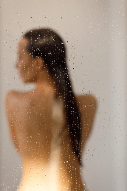Jovem sob os pingos de água no banho de prazer Linda garota sob o spray de água Molhada através de gotas de vidro foco seletivo