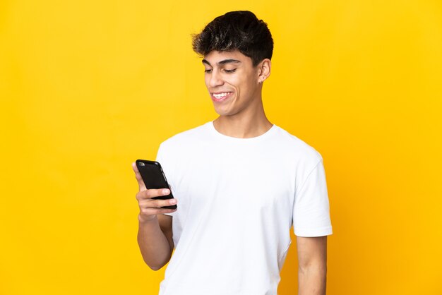 Jovem sobre fundo amarelo isolado enviando uma mensagem ou e-mail com o celular