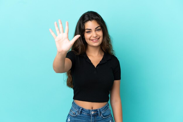 Foto jovem sobre fundo azul e verde posando com os braços no quadril e sorrindo