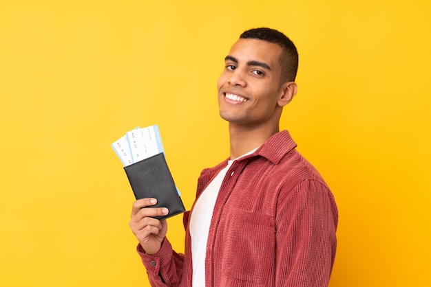 Jovem sobre parede amarela isolada feliz em férias com bilhetes de avião e passaporte