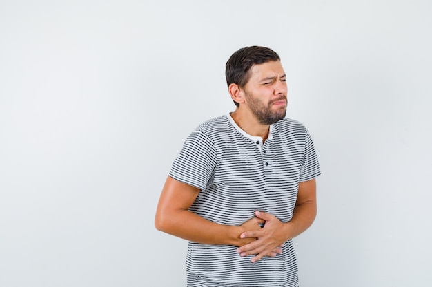 Jovem sofre de dor de estômago em t-shirt e parece incomodado, vista frontal.