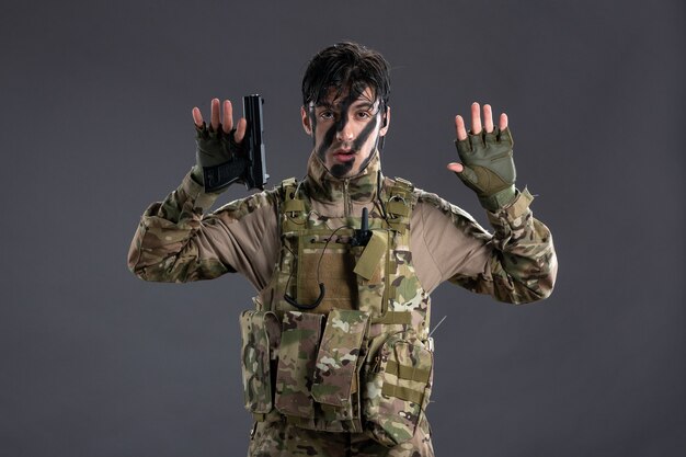 Jovem soldado se rendendo camuflado com arma na parede escura