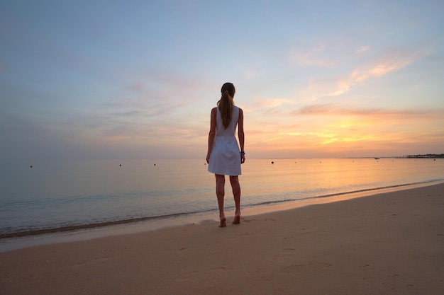 Jovem solitária em pé na praia de areia à beira-mar aproveitando a noite tropical quente