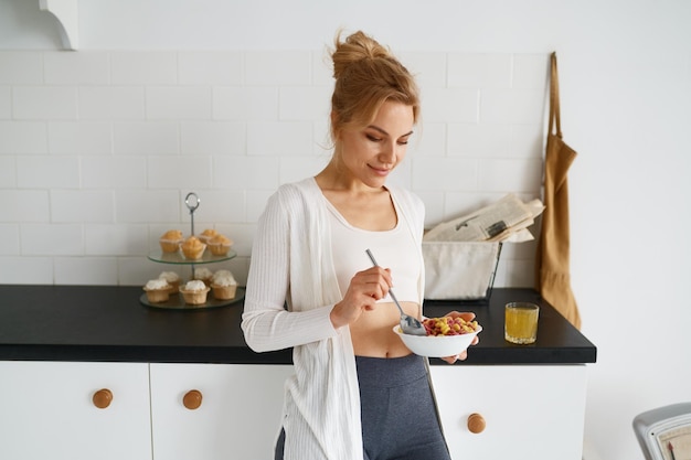 Jovem sonhadora comendo cereais com leite na cozinha de casa