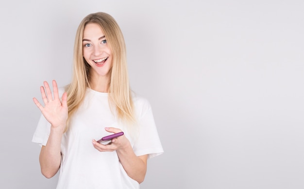 Jovem sorridente, acenando a mão segurando o telefone móvel.