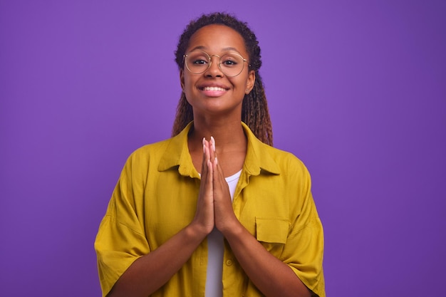 Jovem sorridente afro-americana olha para a câmera e faz gesto de oração