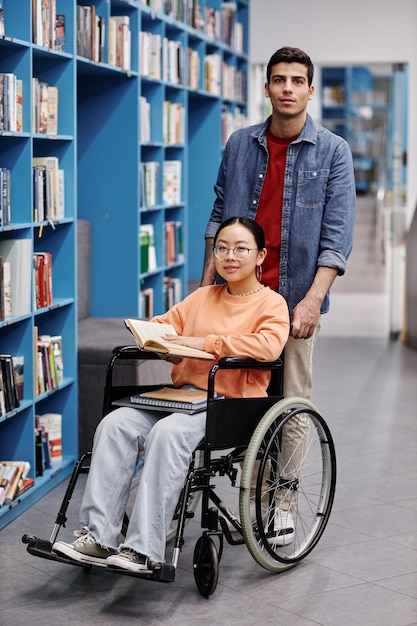 Jovem sorridente ajudando aluna com deficiência na biblioteca