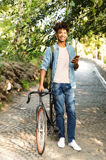 Jovem sorridente ao ar livre, caminhando de bicicleta