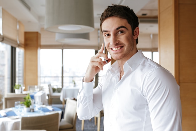 Jovem sorridente bonito falando pelo telefone móvel