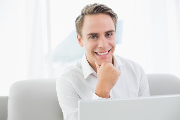 Jovem sorridente casual usando laptop no sofá