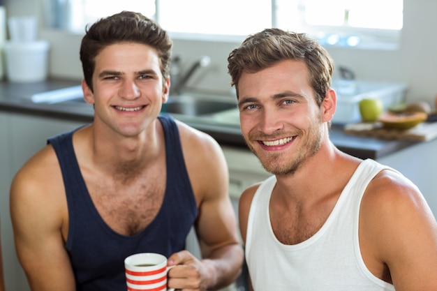 Jovem sorridente com amigo segurando a xícara de café em casa