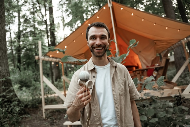 Jovem sorridente com barba por fazer gosta de jogar kendama no local de acampamento, brinquedo de habilidade tradicional. jogo da taça e da bola. brinquedo de madeira. millennial with japanees toy entretendo amigos em glamping de verão