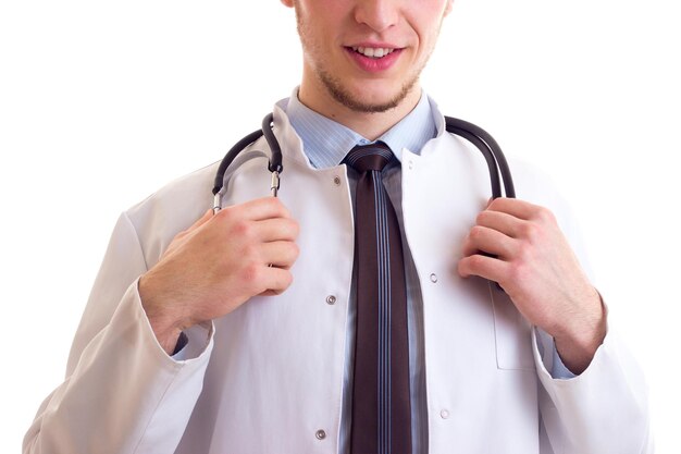 Jovem sorridente com cabelo castanho em gravata de camisa azul e vestido de médico branco com estetoscópio