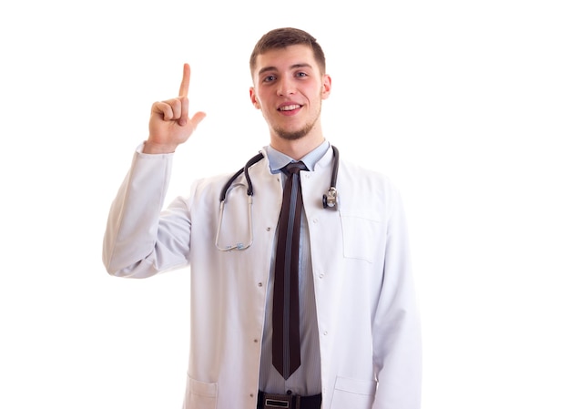 Jovem sorridente com cabelo castanho em gravata de camisa azul e vestido de médico branco com estetoscópio