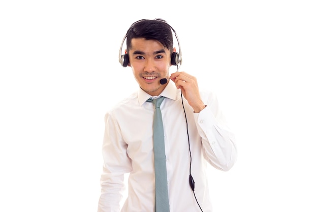 Jovem sorridente com cabelo escuro na camisa branca com gravata azul usando fones de ouvido no estúdio