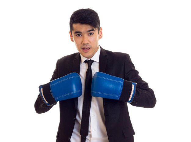 Jovem sorridente com cabelo preto na camisa branca e smoking preto com gravata e luvas de boxe azuis