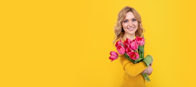 Jovem sorridente com flores de tulipa de primavera em fundo amarelo mulher isolada rosto retrato bandeira com mock up espaço de cópia