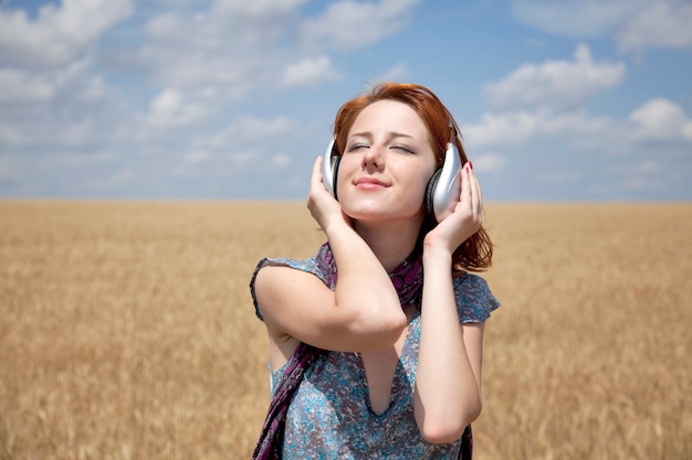 Jovem sorridente com fones de ouvido no campo de trigo.