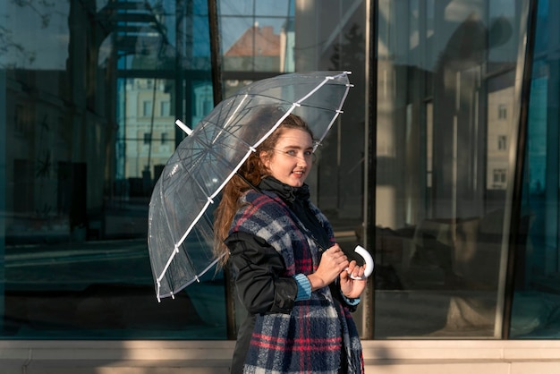 Jovem sorridente com guarda-chuva transparente no dia ensolarado de outono Jovem atraente andando na cidade