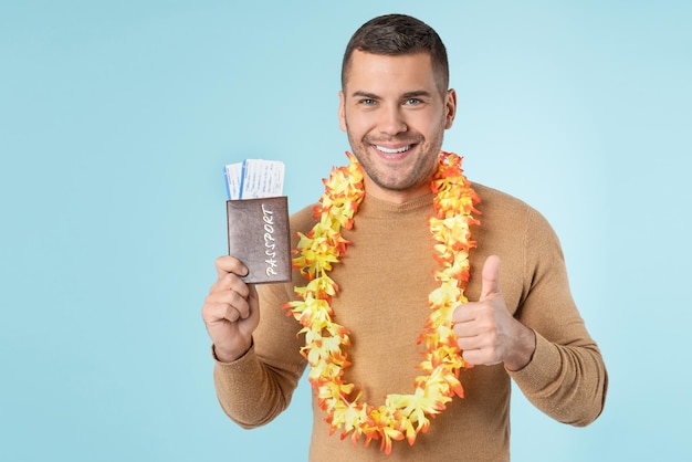 Jovem sorridente com passaporte e bilhetes posando isolado no fundo da parede azul