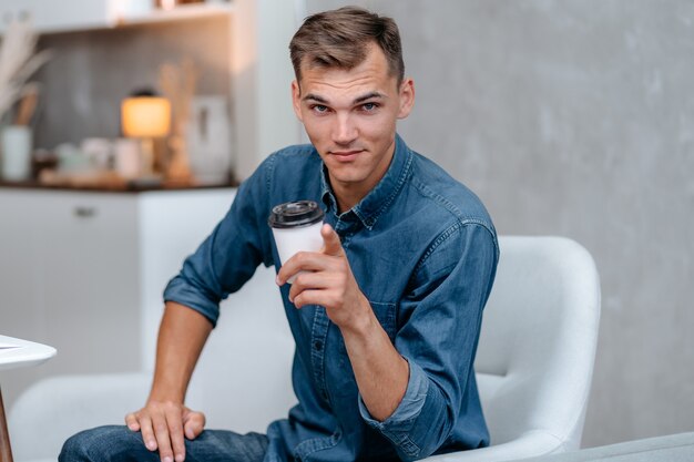 Jovem sorridente com uma xícara de café apontando para você. vida domestica.