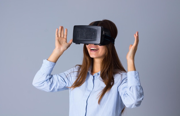 Jovem sorridente de camisa azul usando óculos VR em fundo cinza no estúdio