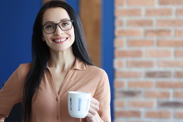 Jovem sorridente de óculos segurando uma caneca com café