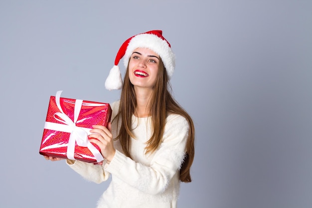 Jovem sorridente de suéter branco com chapéu vermelho de natal segurando presentes no estúdio