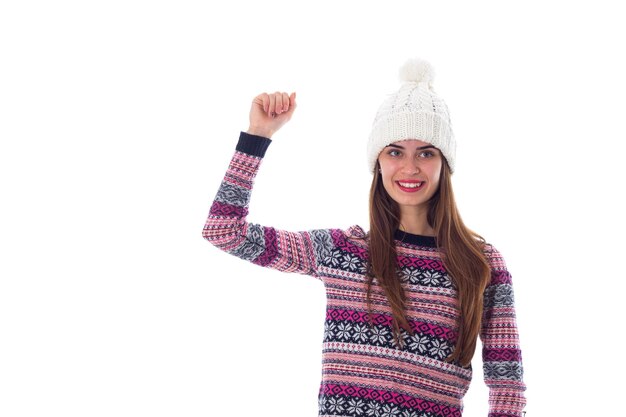 Jovem sorridente de suéter roxo e chapéu branco mostrando punho em fundo branco no estúdio