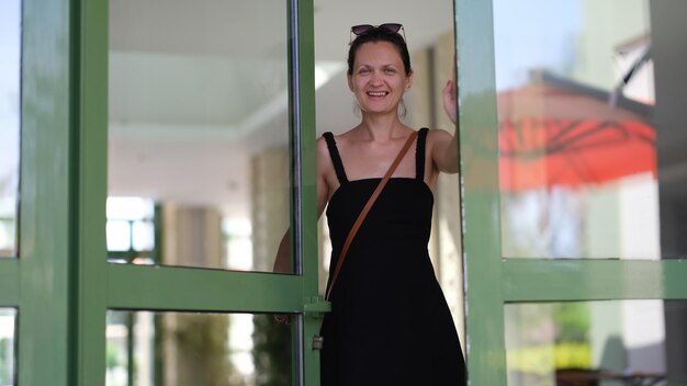 Jovem sorridente de vestido preto entrando na porta de vidro