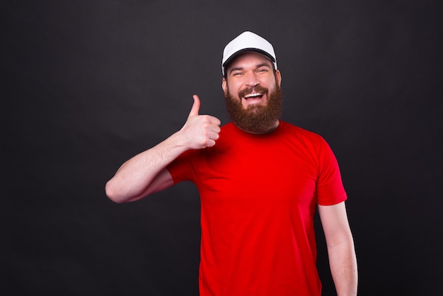 jovem sorridente e alegre em uma camiseta vermelha aparecendo o polegar sobre o preto