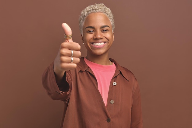 Jovem sorridente e amigável mulher afro-americana mostrando os polegares para cima fica no estúdio