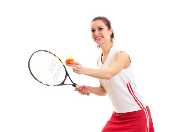 Jovem sorridente em camisa esportiva e saia vermelha com rabo de cavalo castanho segurando raquete de tênis