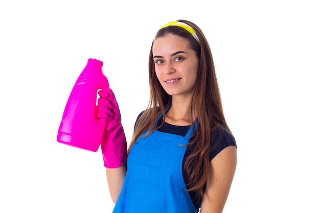 Foto jovem sorridente em camiseta azul e avental com luvas cor de rosa segurando detergente no estúdio