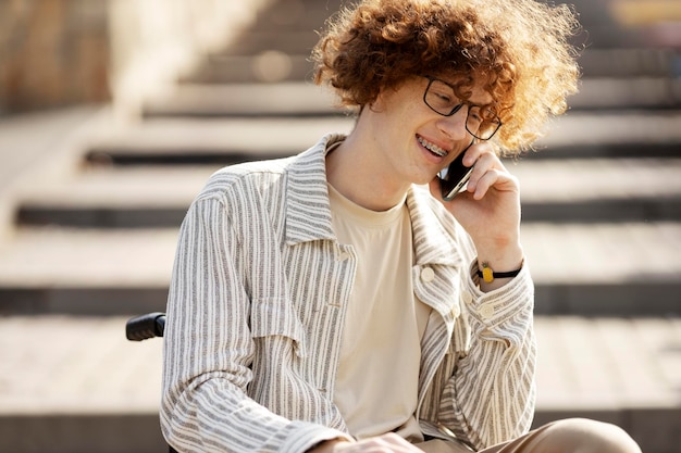 Jovem sorridente em óculos em uma cadeira de rodas falando em um telefone celular