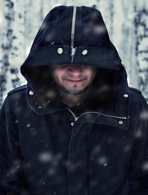jovem sorridente em roupas escuras de inverno quente em um clima de neve em um capuz em um fundo