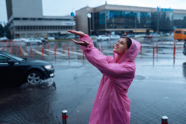 Jovem sorridente em uma capa de chuva rosa, aproveitando um dia chuvoso