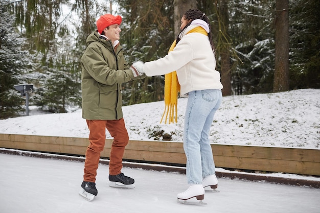 Jovem sorridente ensinando a mulher a patinar na pista de patinação ao ar livre