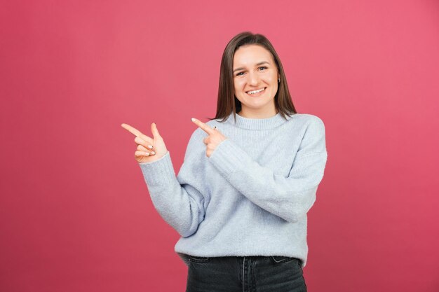 Jovem sorridente está apontando de lado sobre fundo rosa em um estúdio