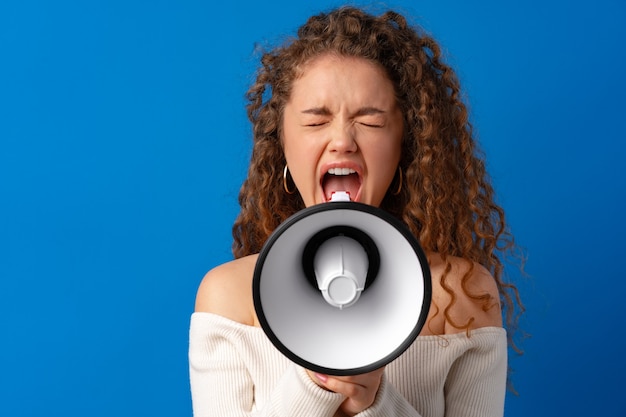 Foto jovem sorridente expressiva mulher caucasiana gritando no megafone contra um fundo azul