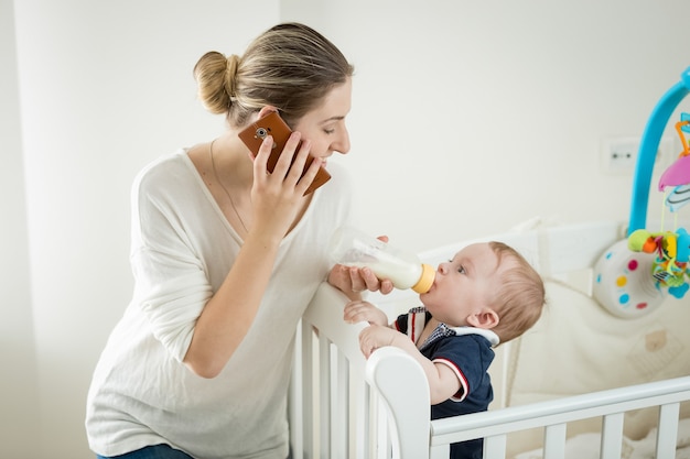 Jovem sorridente falando ao telefone enquanto alimenta seu filho bebê