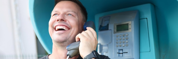 Jovem sorridente falando na cabine telefônica na comunicação de rua pelo conceito de telefone fixo