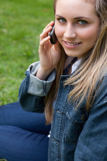 Jovem sorridente falando no telefone enquanto está sentado em um parque