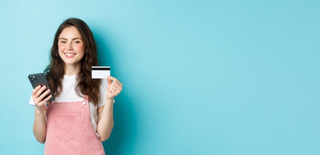 Jovem sorridente fazendo compras online com cartão de crédito e smartphone nas mãos