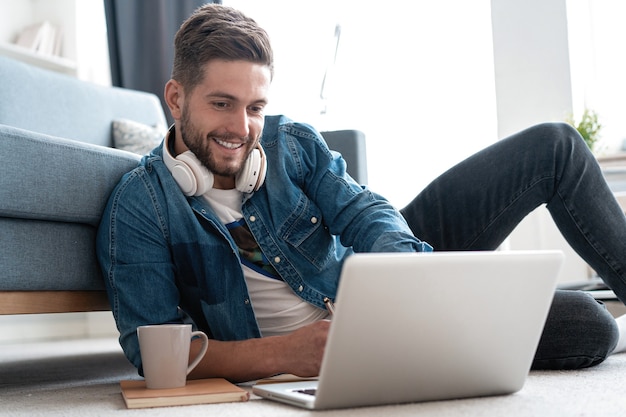 Jovem sorridente fazendo videochamada com amigos em sua casa moderna. Conceito de empresários felizes