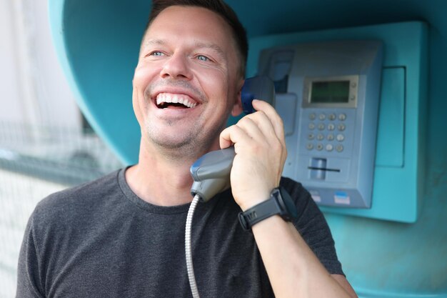 Jovem sorridente feliz falando no telefone, no conceito de comunicação telefônica de cidade de cabine