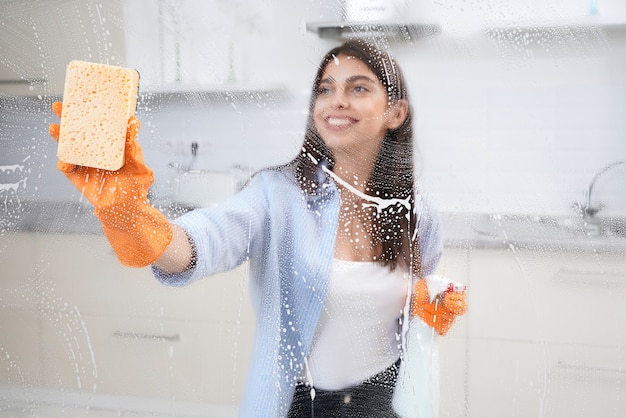 Jovem sorridente lavando janela em casa