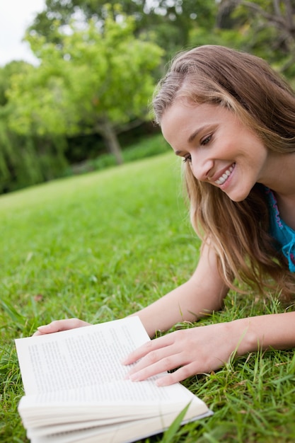 Jovem sorridente lendo um livro enquanto deitava um parque