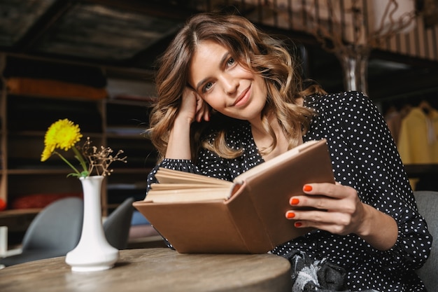 Jovem sorridente lendo um livro enquanto está sentado no café