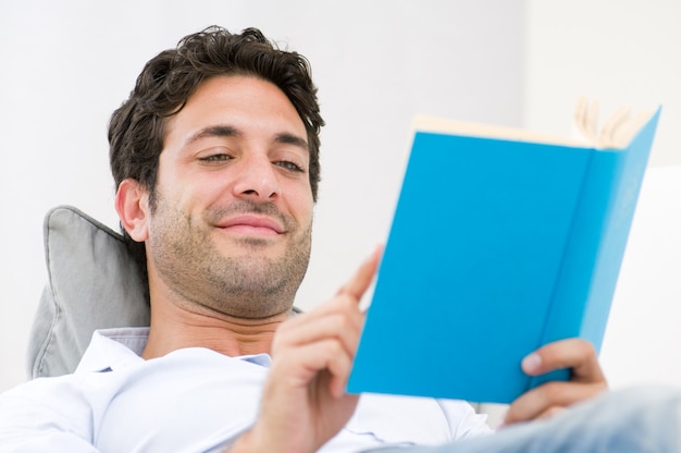 Jovem sorridente lendo um livro enquanto relaxa no sofá